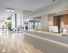 Bright reception desk with marble flooring, white counters, decorative plants and pendant lighting at Hotel Sallés Ciutat del Prat.
