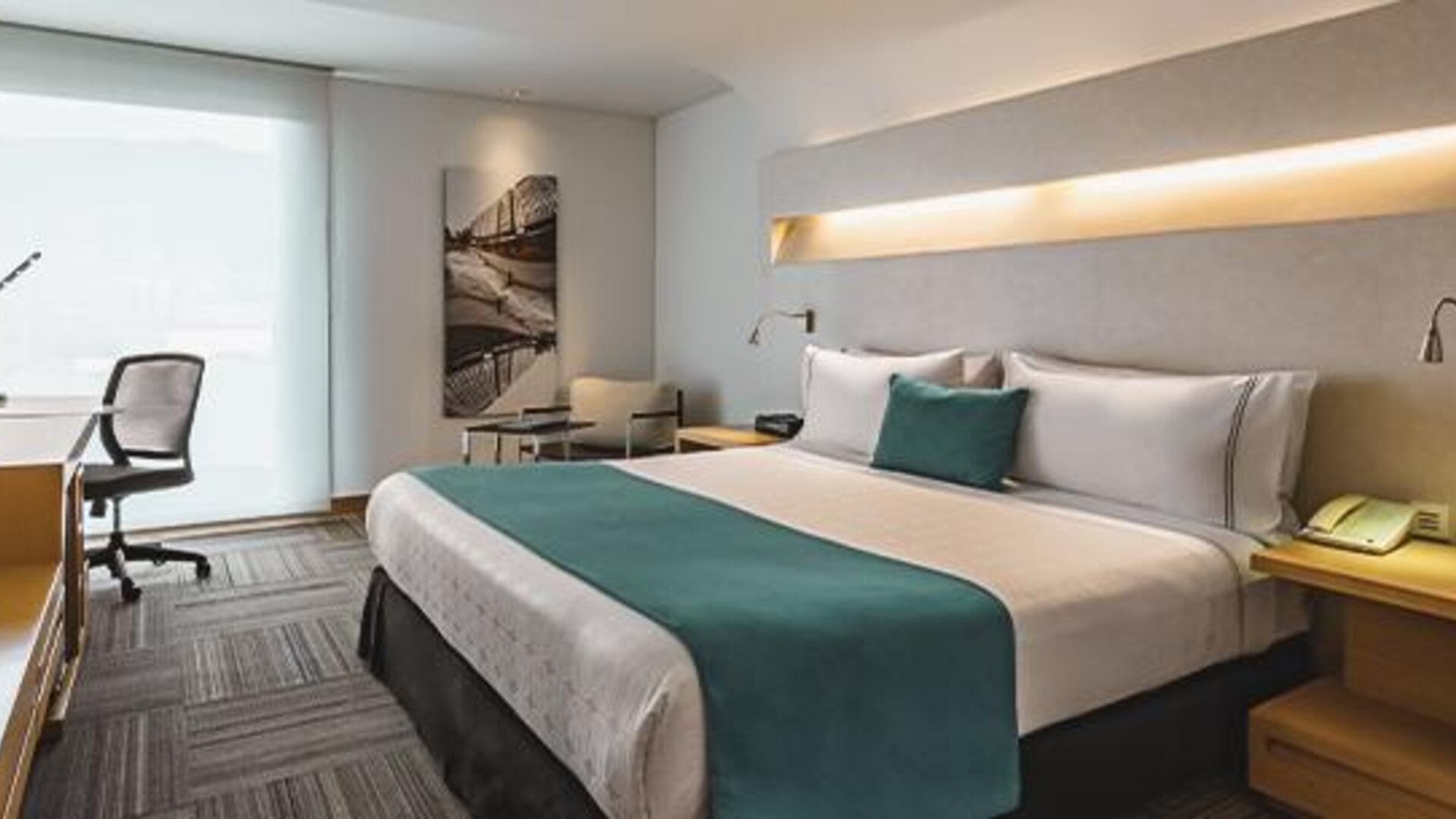 Guest room with king-size bed, teal cushions, bedside furniture and workspace at Sonesta Hotel Bogotá.