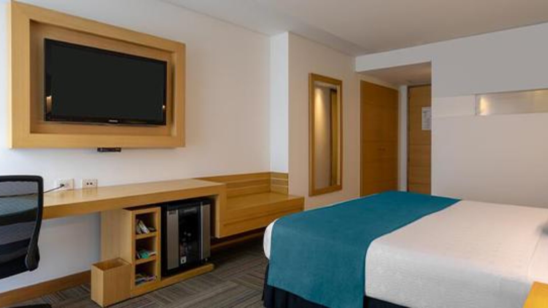 Guest room with white bedding, teal bed runner, wall-mounted television and work desk at Sonesta Hotel Bogotá.