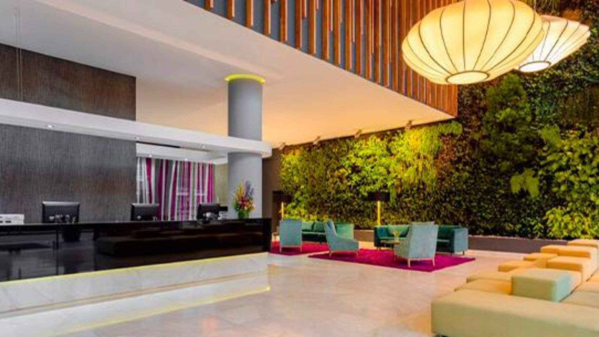 Reception area with dark front desk, green living wall, orange seating and decorative pendant lights at Sonesta Hotel Bogotá.