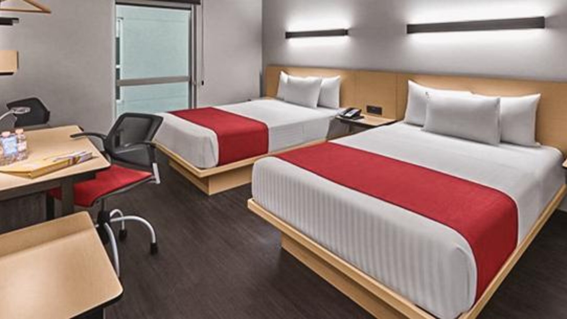 Guest room with two beds, red bed runners, wooden headboards, bedside lighting and a work desk at City Express by Marriott CDMX La Villa.