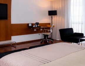 Guest room with large bed, wall-mounted television, desk, black lounge chairs and floor-to-ceiling curtains at Design Suites Buenos Aires.
