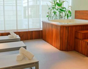 Spa relaxation area with white loungers, rolled towels, wooden hot tub and large windows at Design Suites Buenos Aires.