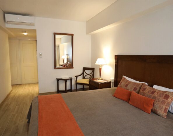 Guest room with king bed, patterned cushions, orange bed runner, wooden headboard and bedside lamps at HR Esmeralda Luxor.