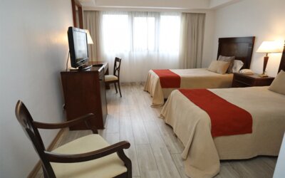 Twin guest room with two beds, orange runners, wooden furniture, television and large curtained windows at HR Esmeralda Luxor.
