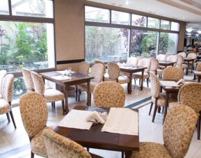 Dining room with patterned upholstered chairs, wooden tables, white tiled floors and large garden-facing windows at HR Esmeralda Luxor.