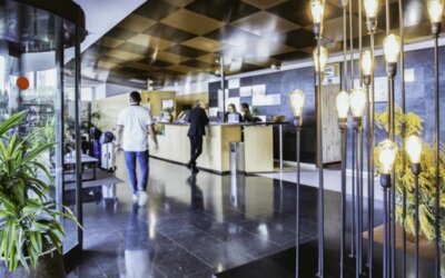 Hotel reception area with front desk, dark stone walls, decorative pendant lights and a glass revolving door at Hotel Best Western PLUS Alfa Aeropuerto.
