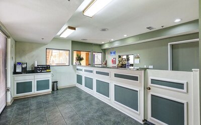 Reception area at Buena Vista Inn featuring a long white and sage-green front desk, tiled flooring, overhead lighting, and a beverage station for guests.