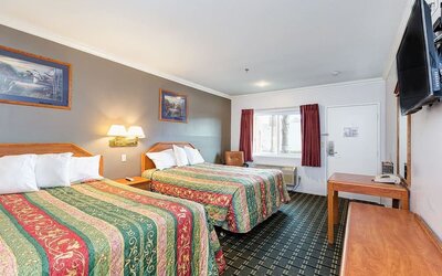 Guest room at Buena Vista Inn featuring two beds with colorful patterned bedspreads, wooden headboards, wall-mounted lighting, flat-screen television, writing desk, and window with burgundy curtains.