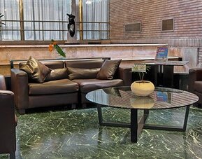 Lounge with dark leather sofas, armchairs, glass coffee table and green marble flooring at Hotel Regente Palace.