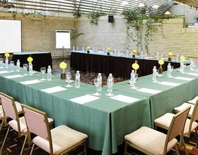 Conference room with green-covered tables arranged in a U-shape, chairs, place settings and projection screens at Hotel Regente Palace.