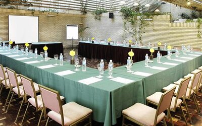 Conference room with green-covered tables arranged in a U-shape, chairs, place settings and projection screens at Hotel Regente Palace.