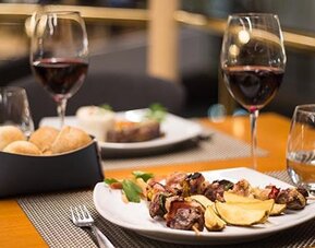 Restaurant table set with plated food, bread rolls, wine glasses and folded napkins at Hotel Regente Palace.