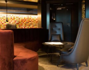 Hotel lounge with curved burgundy sofa, grey armchairs, round coffee table and illuminated decorative wall at Hotel Silken Saaj Las Palmas.