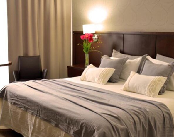 Guest room with a king bed, grey runner, layered pillows, bedside tables and warm lighting at Ian Hotel.