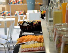Breakfast buffet with pastries, sliced cold meats, juice bottles and jars of preserves beside dining tables at Ian Hotel.