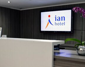 Hotel reception desk with white counter, wall-mounted Ian Hotel logo screen and purple orchids at Ian Hotel.