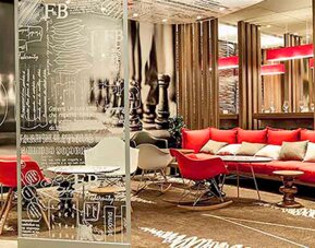 Hotel lobby with red sofas, decorative glass partitions, wooden slat dividers and patterned carpeting at Ibis Lima Reducto Miraflores.