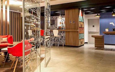 Reception and lounge area with wooden counters, blue wall panels, pendant lighting and red seating at Ibis Lima Reducto Miraflores.