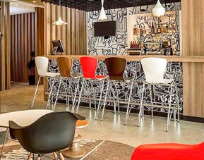 Hotel lounge with red sofas, colorful chairs, round coffee tables and patterned carpet at Ibis Lima Reducto Miraflores.