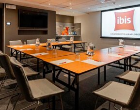 Meeting room with conference tables, grey chairs, water glasses and a presentation screen at Ibis Lima Reducto Miraflores.