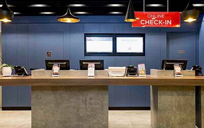 Hotel reception with long wooden counter, blue wall panels, computer stations and hanging pendant lights at Ibis Lima Reducto Miraflores.