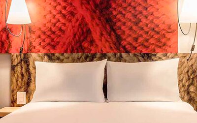 Close view of a double bed with white pillows, red decorative headboard and matching wall lamps at Ibis Lima Reducto Miraflores.