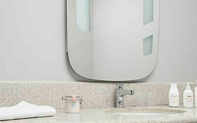 Bathroom vanity with speckled countertop, white sink, wall mirror, toiletries and folded towel at Ibis Lima Reducto Miraflores.
