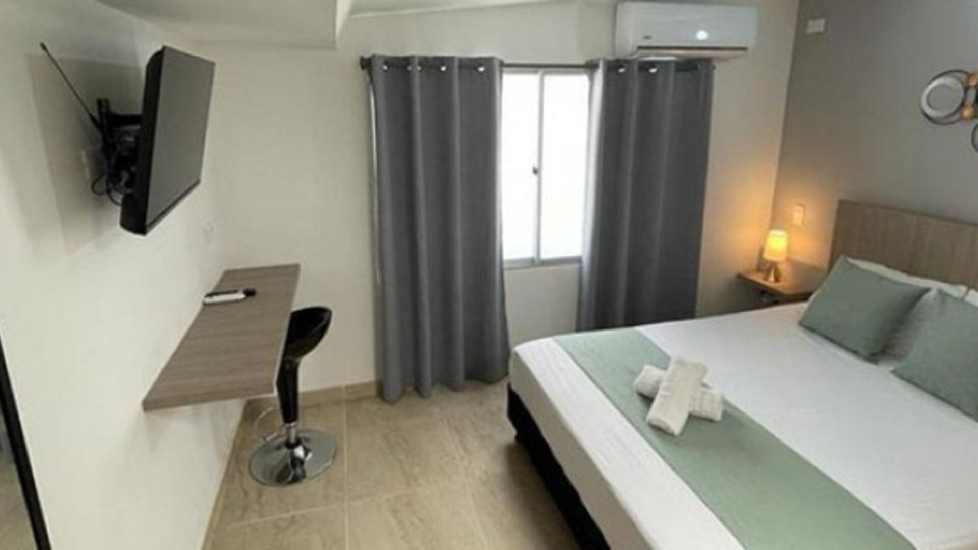 Guest room with double bed, pale green runner and cushions, wall-mounted television, desk and grey curtains at 12 Nights Hotel.