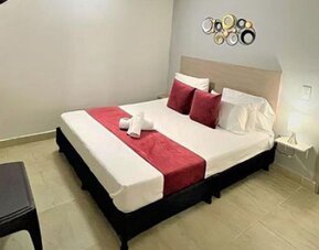 Guest room with double bed, red runner and cushions, wall-mounted television and ensuite bathroom visible through the doorway at 12 Nights Hotel.