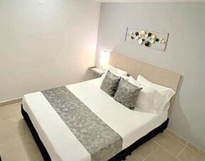 Guest room with double bed, grey patterned runner, matching cushions, bedside table and wall-mounted television at 12 Nights Hotel.