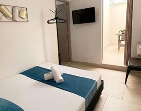 Guest room with bed, teal runner and cushions, wall-mounted television, dressing table and full-length mirror at 12 Nights Hotel.