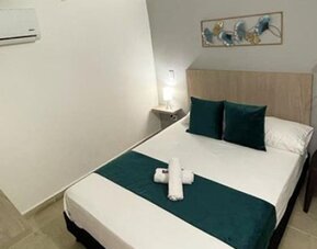 Guest room with double bed, teal bedding accents, wall-mounted television, air conditioner and open clothes rail at 12 Nights Hotel.