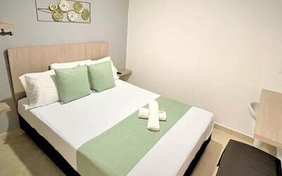 Guest room with double bed, green accent cushions, matching bed runner, wall-mounted television and wooden desk at 12 Nights Hotel.