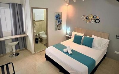 Guest room with double bed, teal runner and cushions, bedside lighting, desk and ensuite bathroom at 12 Nights Hotel.