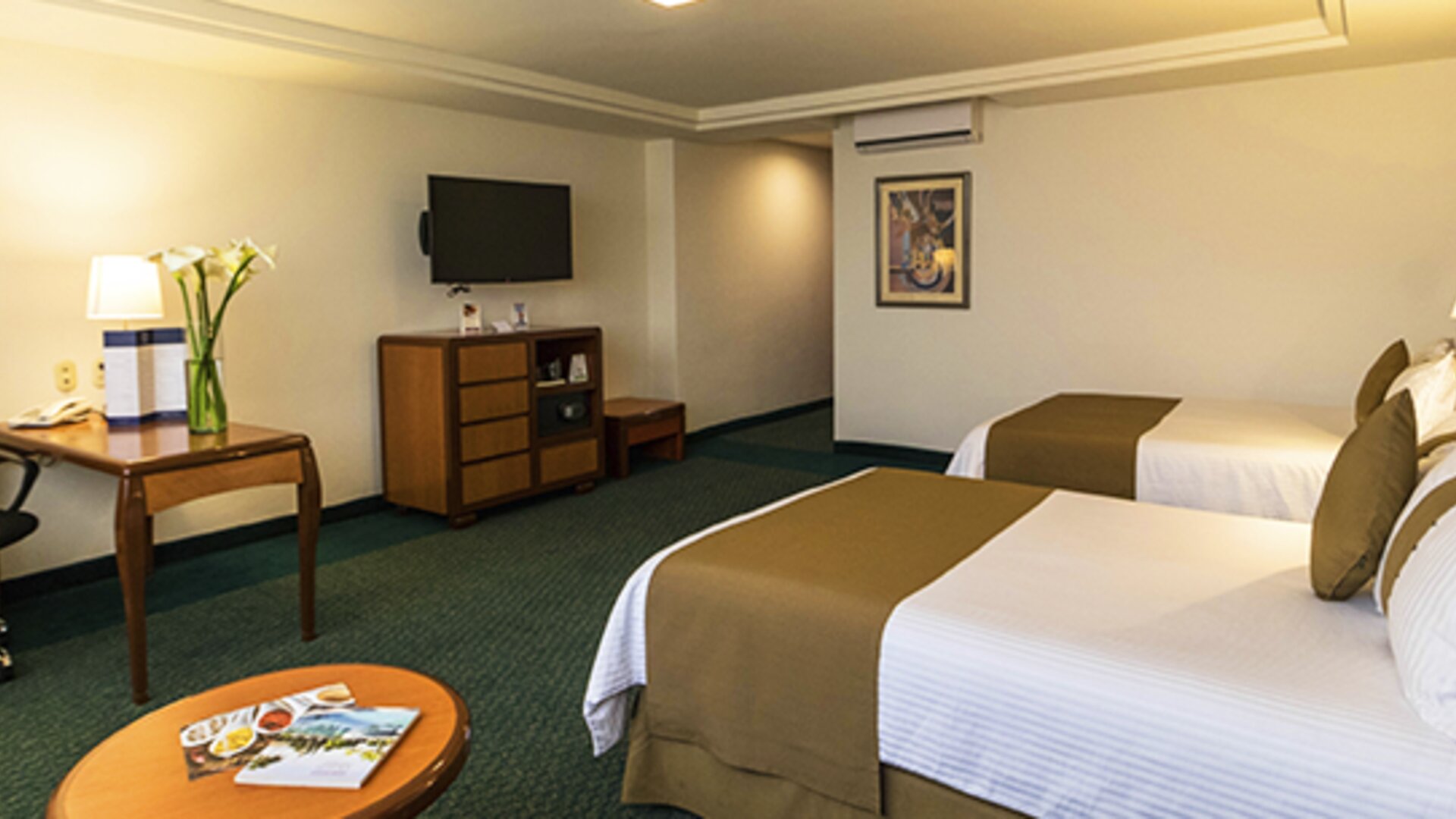 Guest room with two beds, white bedding, green accents, wooden furniture, desk and wall-mounted television at Hotel Misión Toreo Centro De Convenciones.