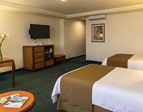 Guest room with two beds, white bedding, green accents, wooden furniture, desk and wall-mounted television at Hotel Misión Toreo Centro De Convenciones.