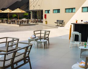 Outdoor seating area with tables, chairs, bar counter and umbrellas on a paved terrace at Hotel Misión Toreo Centro De Convenciones.