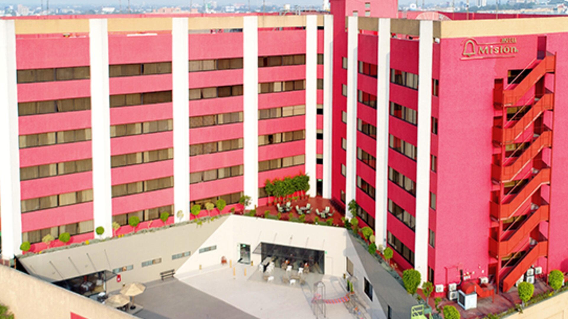 Multi-storey hotel exterior with pink and white façade, green accents and landscaped entrance at Hotel Misión Toreo Centro De Convenciones.