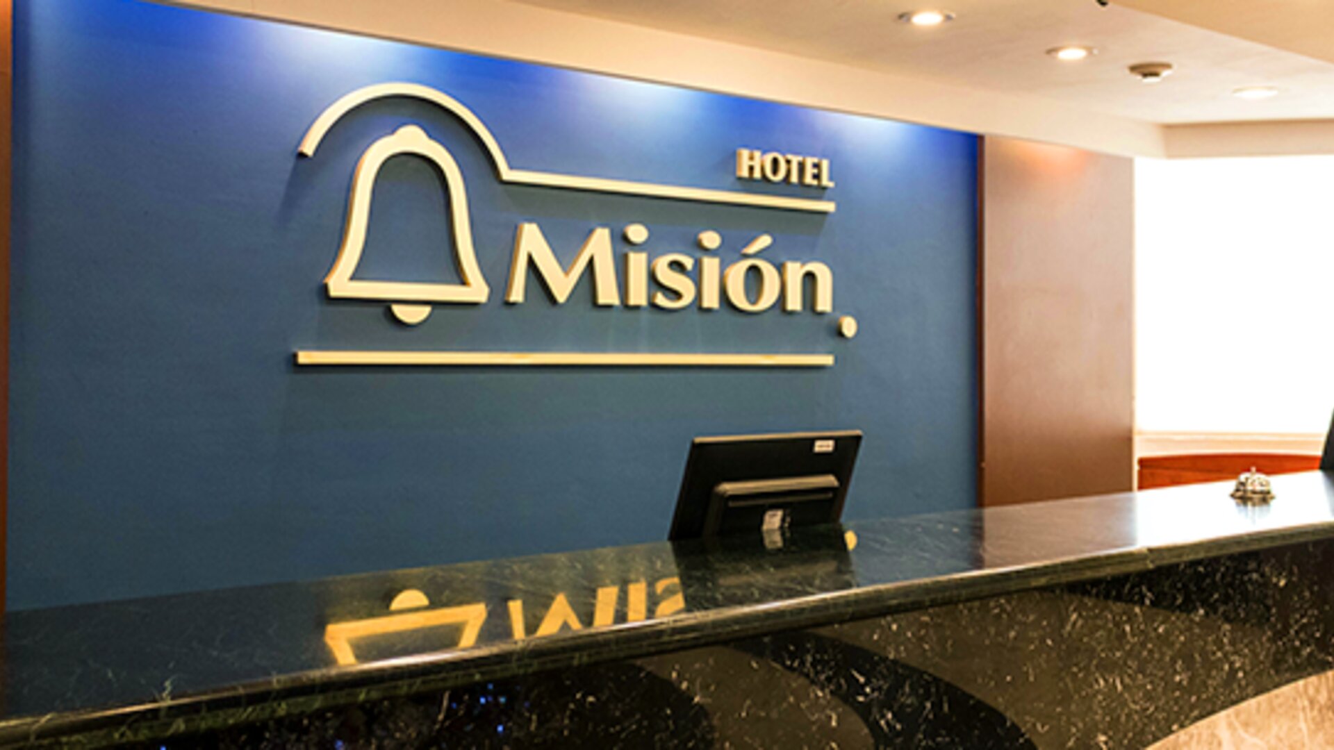 Hotel reception with black marble counter, blue feature wall and gold Hotel Misión signage at Hotel Misión Toreo Centro De Convenciones.