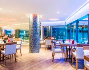 Hotel restaurant with neatly arranged tables, upholstered chairs, pendant lights and floor-to-ceiling windows at Hospedium Princess Hotel Panamá.