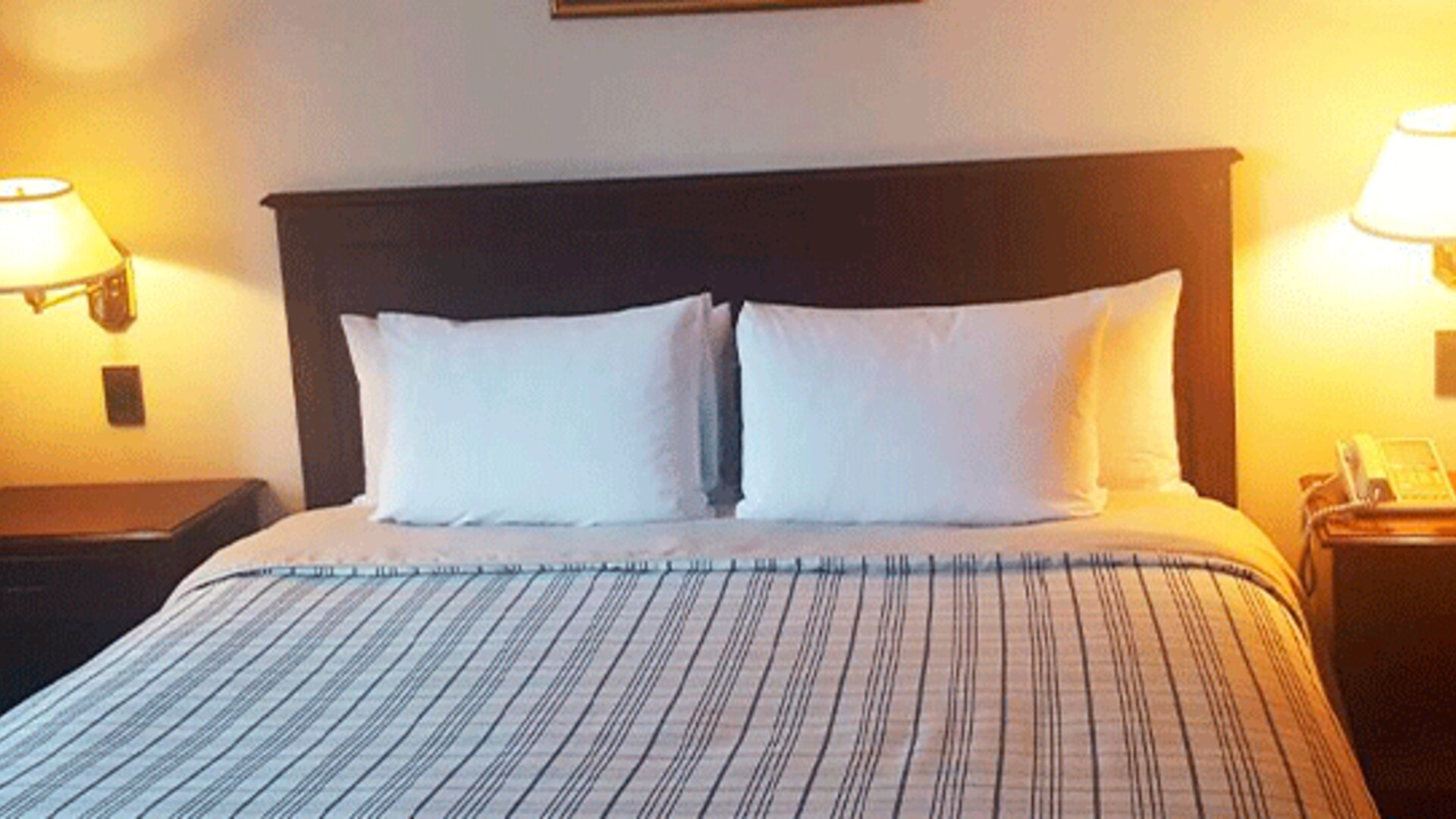 Guest room with double bed, striped bedding, dark wooden headboard and matching bedside tables with lamps at Hospedium Princess Hotel Panamá.