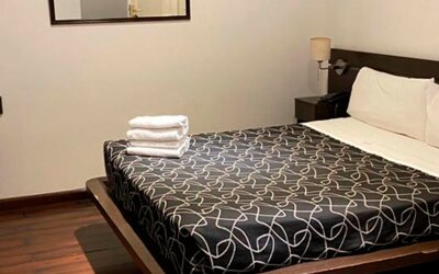 Guest room with double bed, black patterned bedding, folded white towels, bedside table and wall mirror at Bagu Buenos Aires.