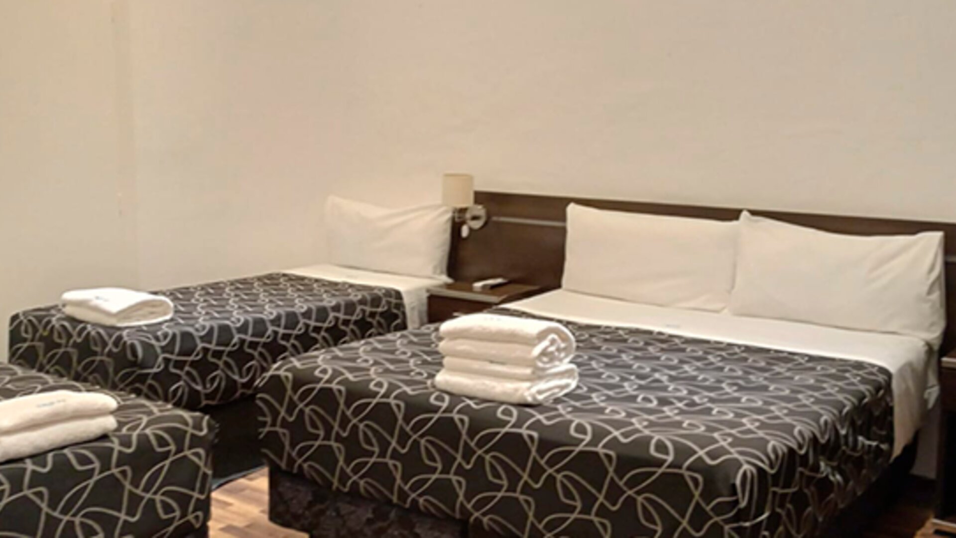 Guest room with one double bed and two single beds, patterned black bedding, white towels and dark bedside furniture at Bagu Buenos Aires.