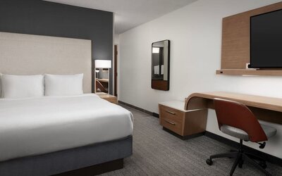 Guest room with a white bed, upholstered headboard, wooden desk, office chair, wall-mounted television and gray carpeting at Courtyard By Marriott Dothan.