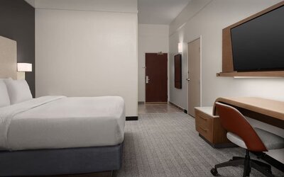 Guest room with white bed, wall-mounted television, wooden desk, office chair and gray carpeting at Courtyard By Marriott Dothan.