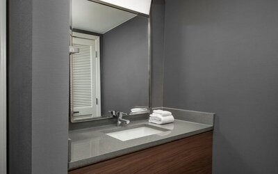 Bathroom vanity with gray countertop, inset sink, large mirror, wooden cabinetry and neatly folded white towels at Courtyard By Marriott Dothan.