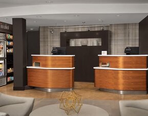Hotel reception area with two curved wooden front desks, computer terminals, a snack display and modern lounge seating at Courtyard By Marriott Dothan.