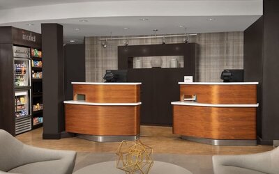 Hotel reception area with two curved wooden front desks, computer terminals, a snack display and modern lounge seating at Courtyard By Marriott Dothan.