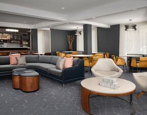 Lobby lounge with gray sectional sofa, upholstered armchairs, round wooden coffee tables and a nearby refreshment counter at Courtyard By Marriott Dothan.